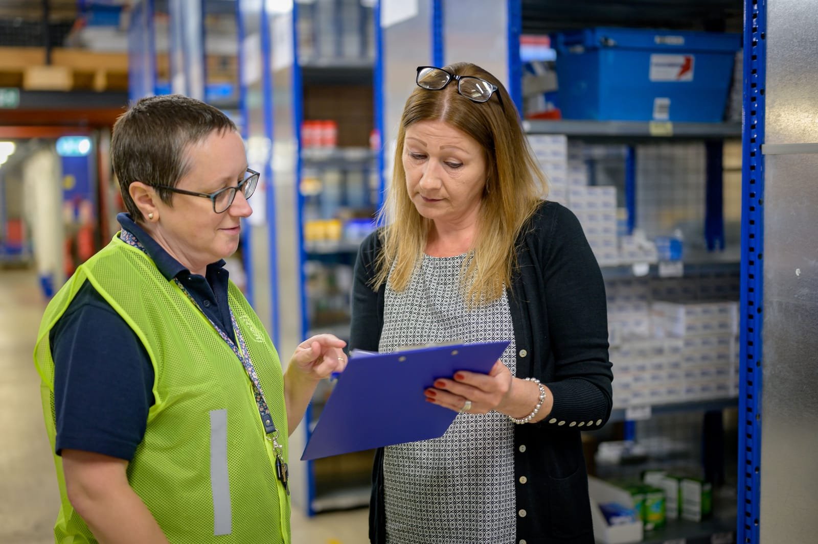 Two workers in a storage facility go through a checklist on a clipboard beside the racking. Photo: Centre for Ageing Better, via Pexels