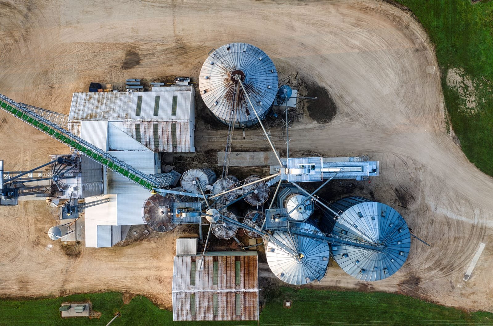 Overhead view of a working grain handling facility: steel storage bins, headhouse, conveyor galleries and truck aprons. Photo: Tom Fisk, via Pexels (Pexels Licence)