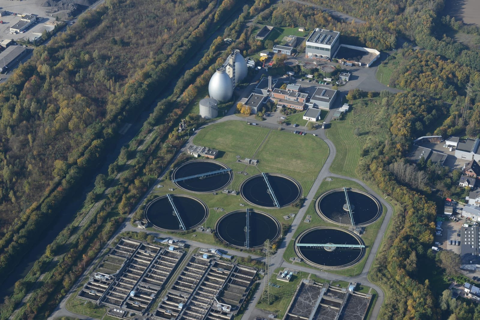 Aerial view of a municipal wastewater treatment plant: circular settling tanks, rows of aeration basins and two egg-shaped sludge digesters. Photo: Hicham Oukachi, via Pexels